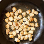 showing how to make chicken pesto pasta recipe by sauteing chicken in a black Dutch oven