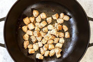 showing how to make chicken pesto pasta recipe by sauteing chicken in a black Dutch oven