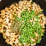 showing how to make chicken pesto pasta recipe by stirring in pesto, peas and Parmesan into the cooked pasta