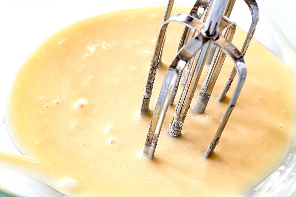 showing how to make overnight breakfast casserole with croissants by beating cream cheese and powdered sugar in a bowl to make a glaze