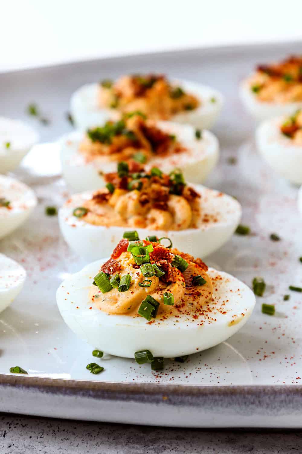 side view of deviled eggs recipe on a platter with bacon and chives