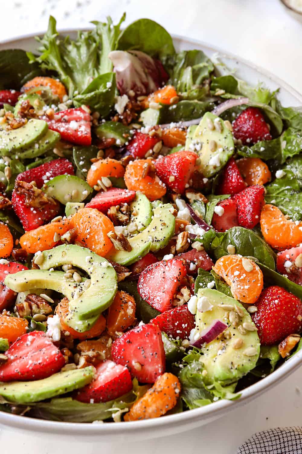strawberry spinach salad recipe in a white bowl with candied nuts, feta and red onions