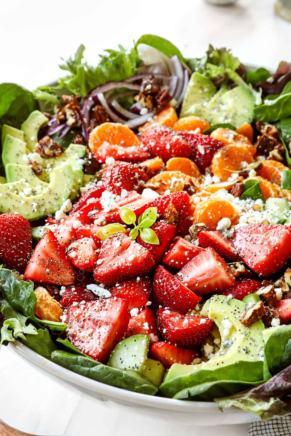 spinach and strawberry salad in a bowl with strawberries, candied nuts, red onions nd feta