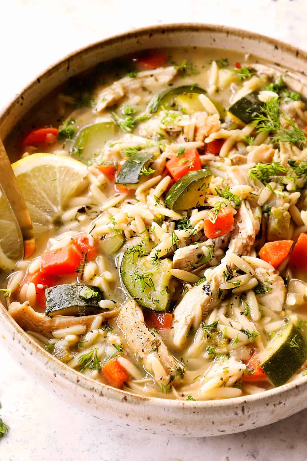 side view of lemon chicken orzo soup with chicken, and fresh dill