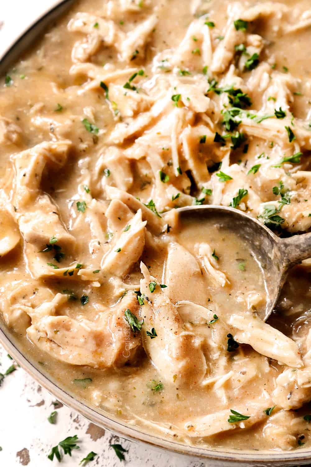 a spoon scooping up crockpot chicken and gravy in a bowl to serve with potatoes