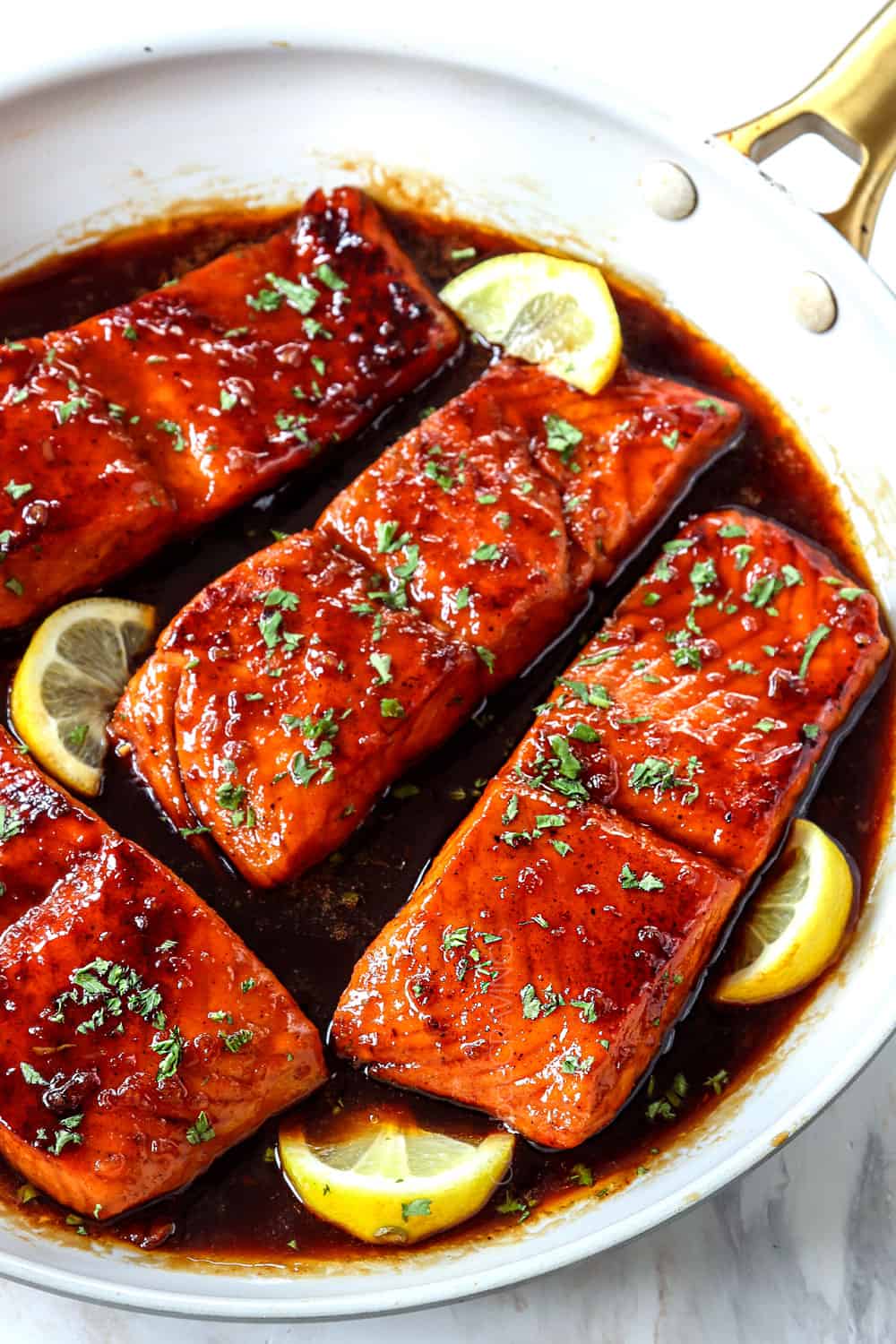 showing how to make honey garlic glazed salmon by drizzling salmon with honey garlic sauce while simmering in the skillet