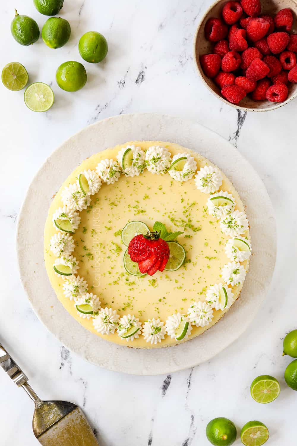 showing how to garnish key lime cheesecake recipe with whipped cream, key limes, key lime zest and a strawberry