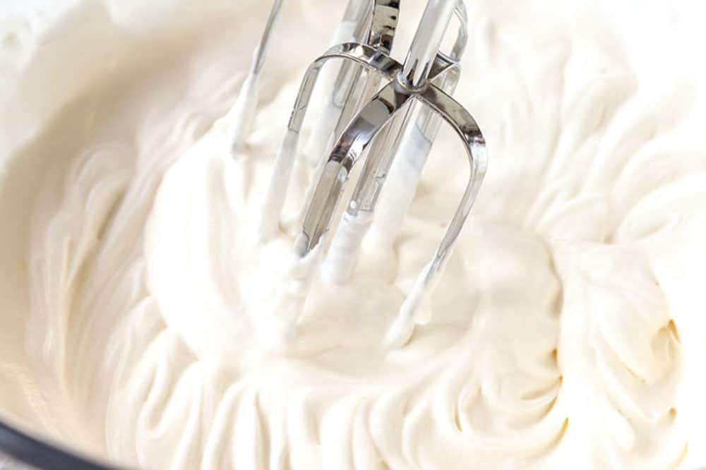 a collage showing how to make key lime cheesecake recipe by making whipping heavy cream and sugar in a bowl to make whipped cream