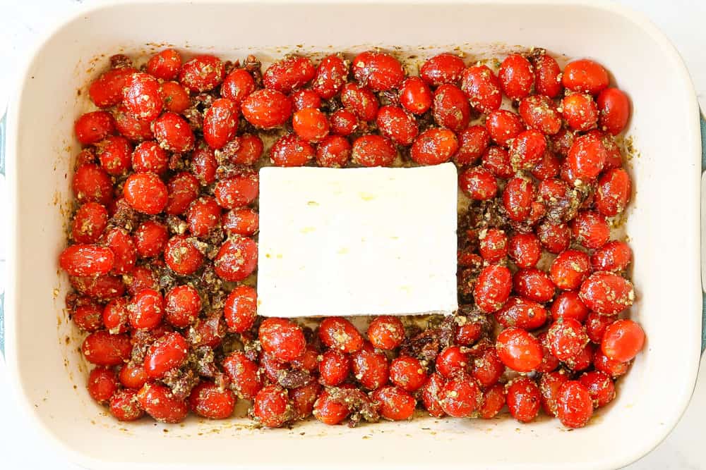 showing how to make tiktok feta pasta by adding feta to the middle of a baking dish surrounded by tomatoes