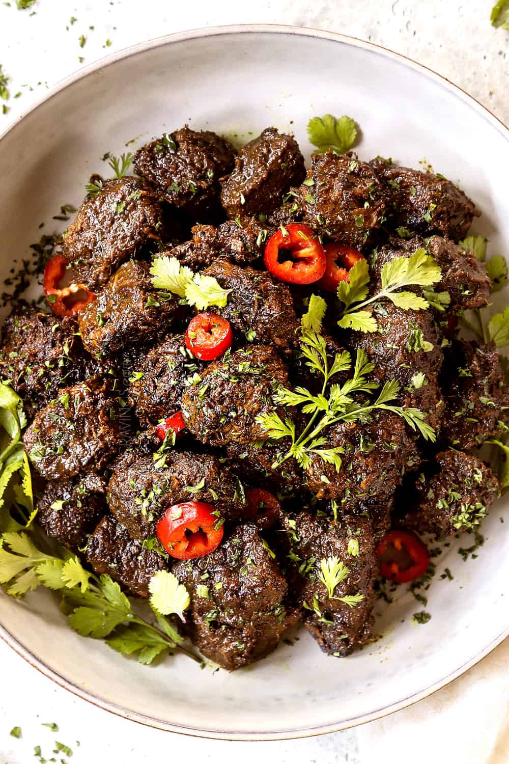 top view of beef rendang in a white bowl garnished with green onions and cilantro