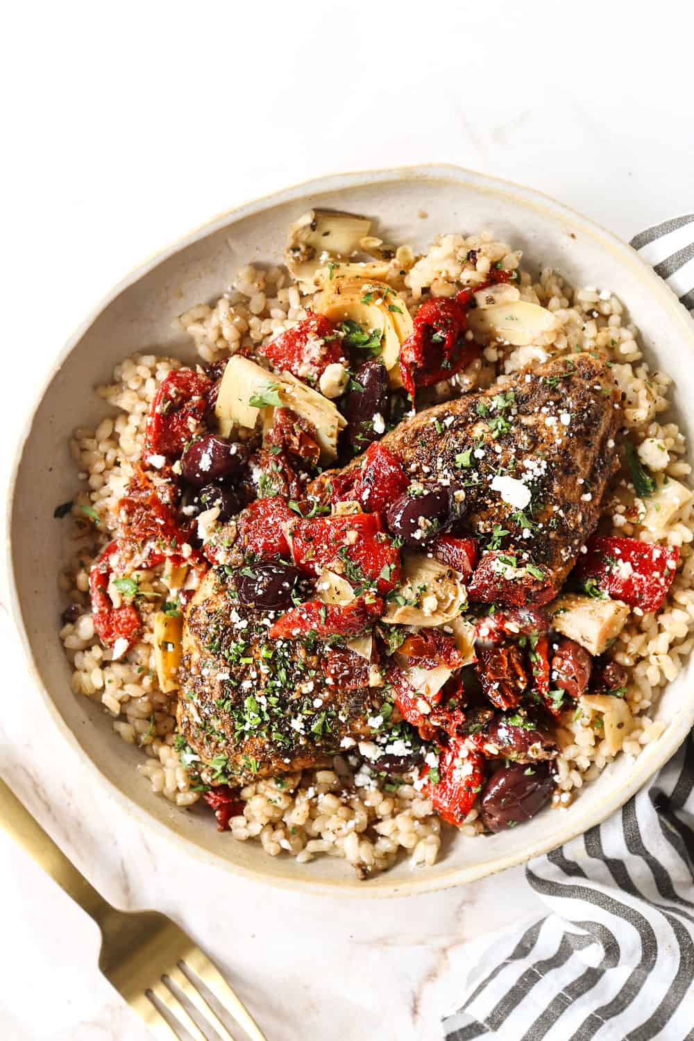 top view of Greek chicken on a plate with rice, tomatoes, olives and feta