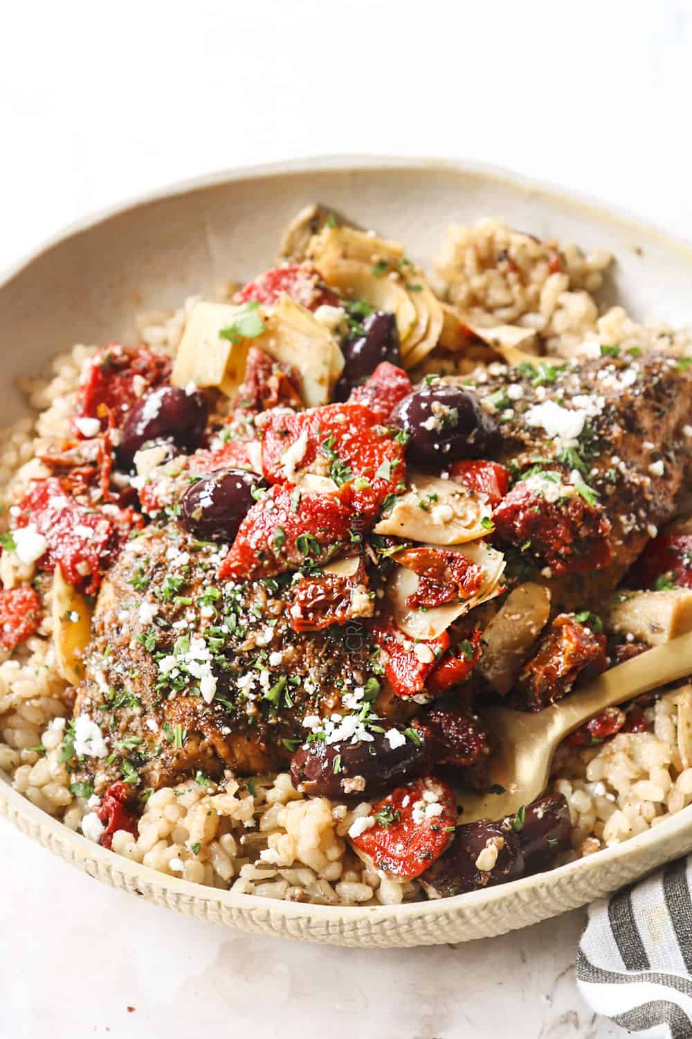 showing how to make Greek chicken recipe by adding to a plate with rice, tomatoes, olives and feta