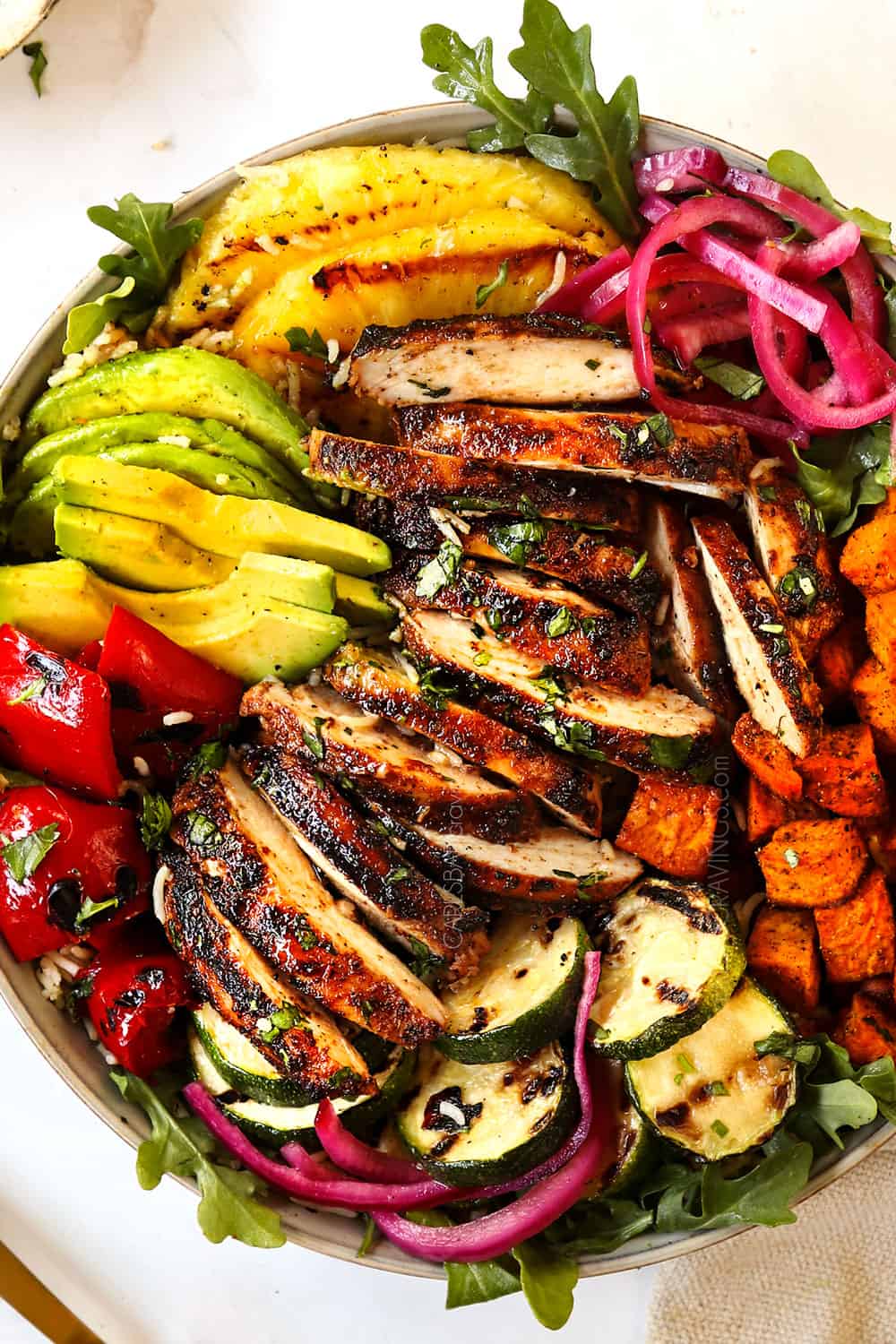 top view of harissa chicken thighs in a bowl with bell peppers, sweet potatoes and pickled red onions showing how to serve the recipe