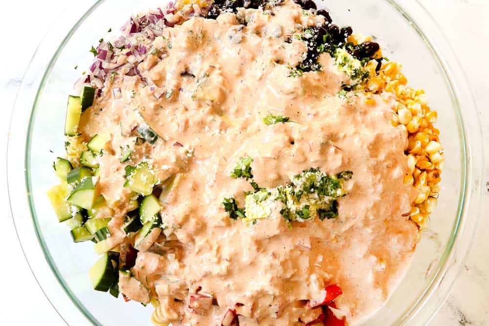 showing how to make Mexican Pasta Salad by adding the pasta salad dressing to the ingredients in a glass bowl