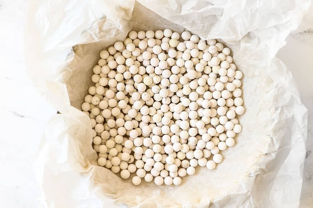 showing how to make Quiche Lorraine by adding pie weights to quiche dough in pan