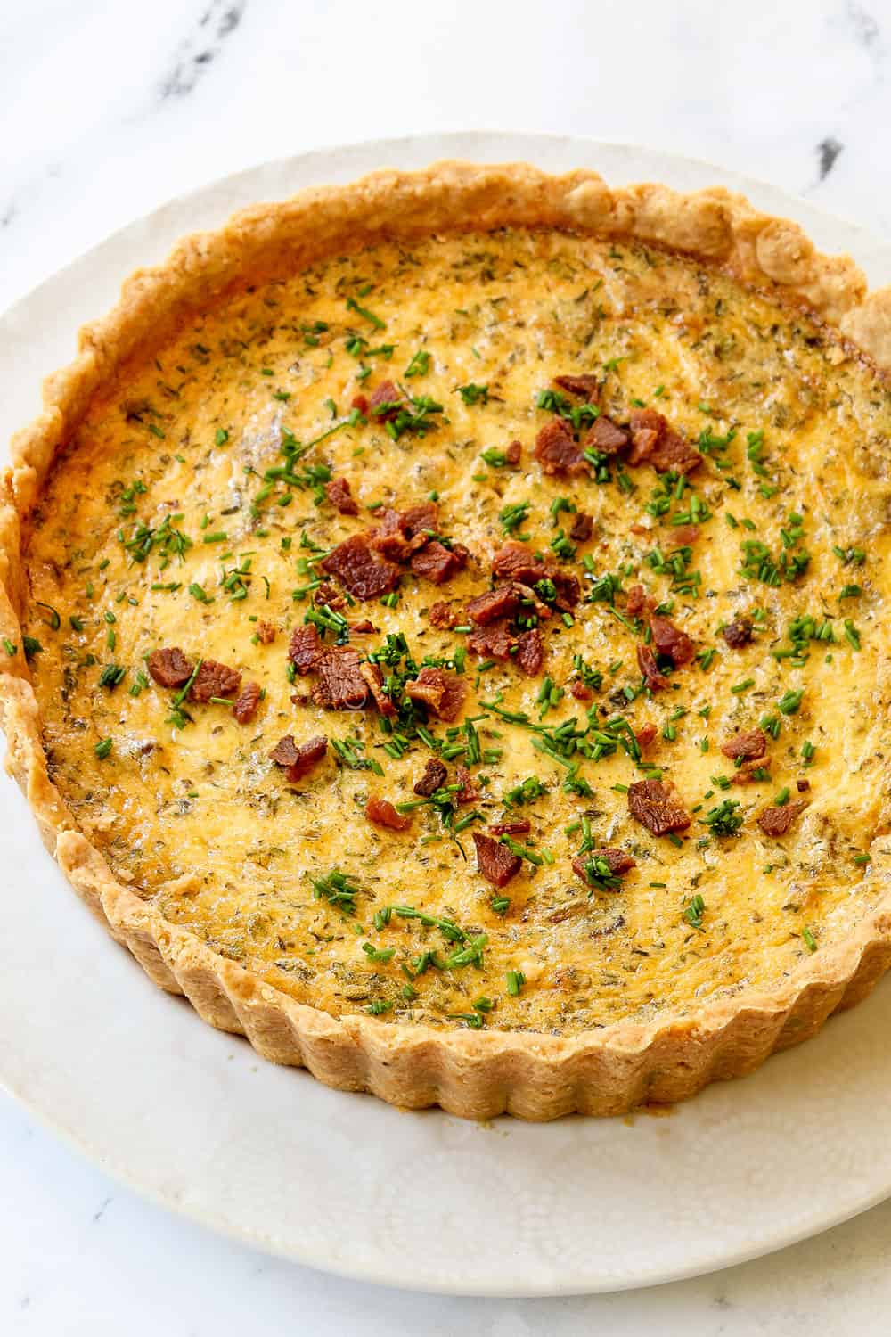 Quiche Lorraine recipe on a white plate garnished with chives on a white plate