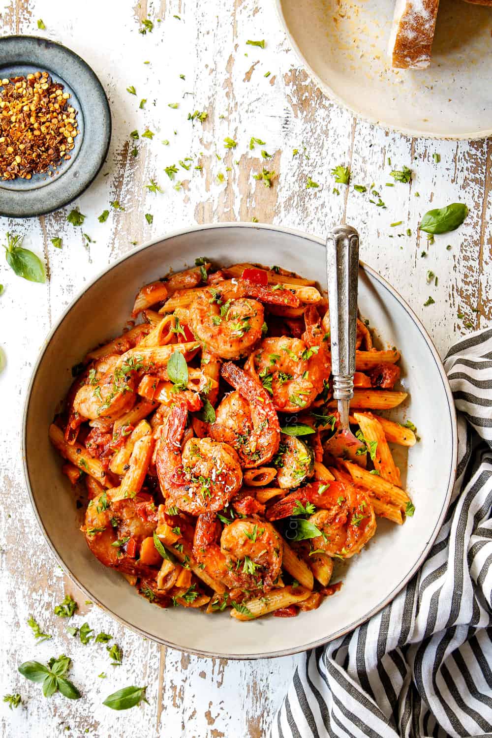 showing how to serve shrimp pasta by adding to a white bowl and garnishing with Parmesan and basil