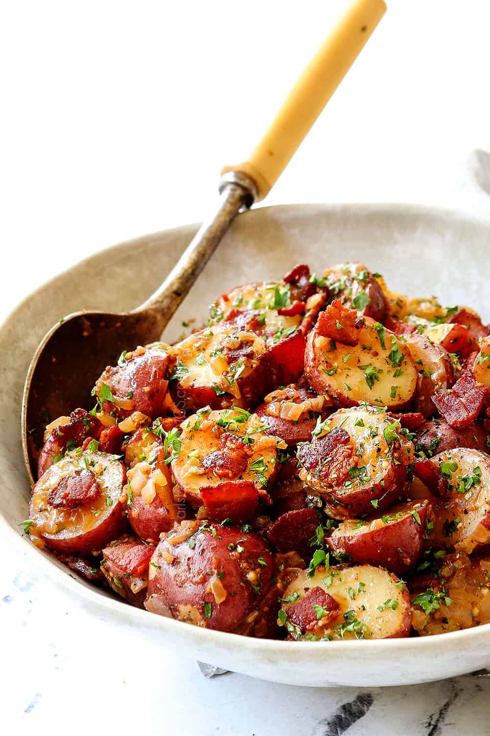 showing how to serve warm German potato salad by adding to a bowl and garnishing with parsley, dill and chives