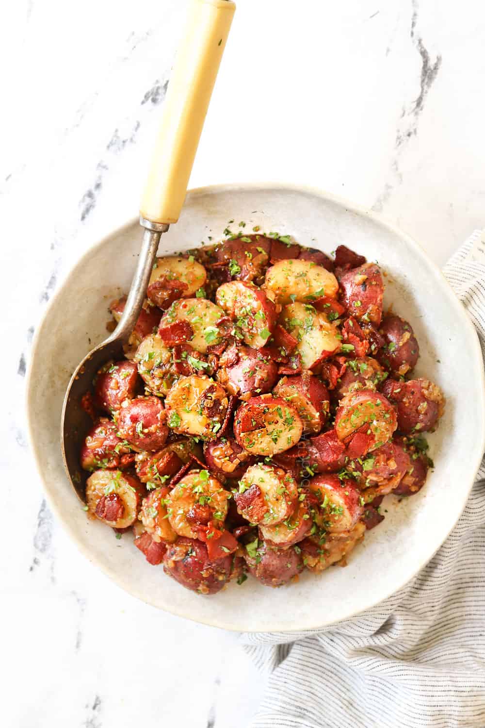 top view of warm German potato salad in a white bowl garnished with parsley