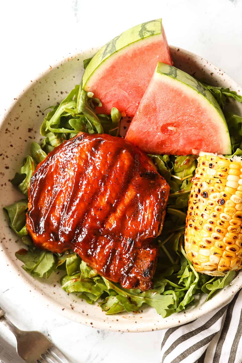 grilled bone in pork chops on a plate with salad, watermelon and grilled corn on the cob