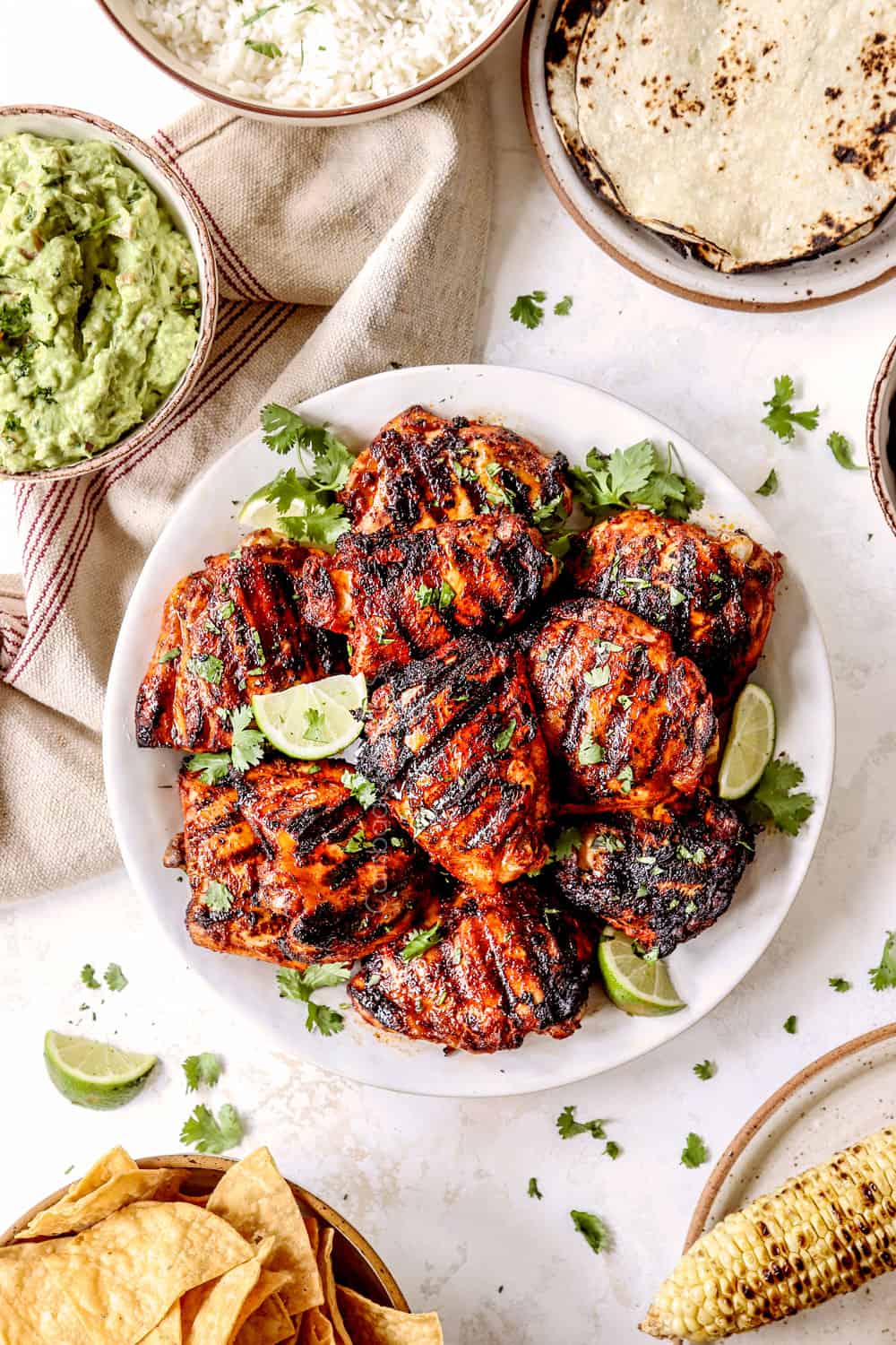 top view of pollo asado and side dishes: corn tortillas, black beans, corn, guacamole and rice