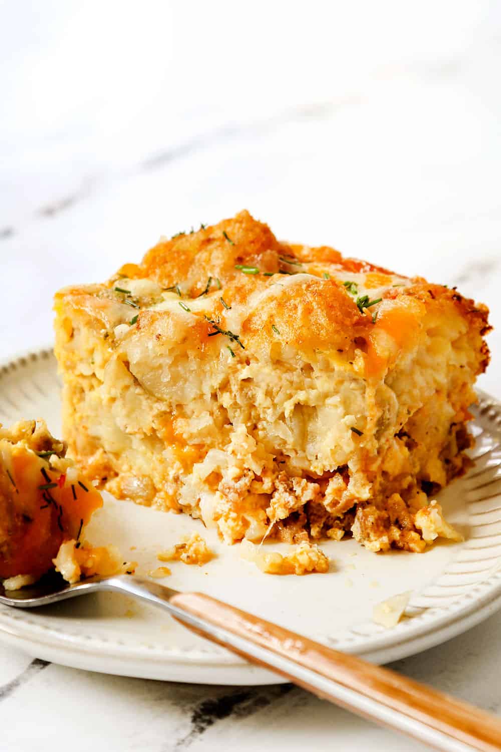 up close of a slice of tater tot breakfast casserole with bite taken out, showing how creamy and cheesy it is