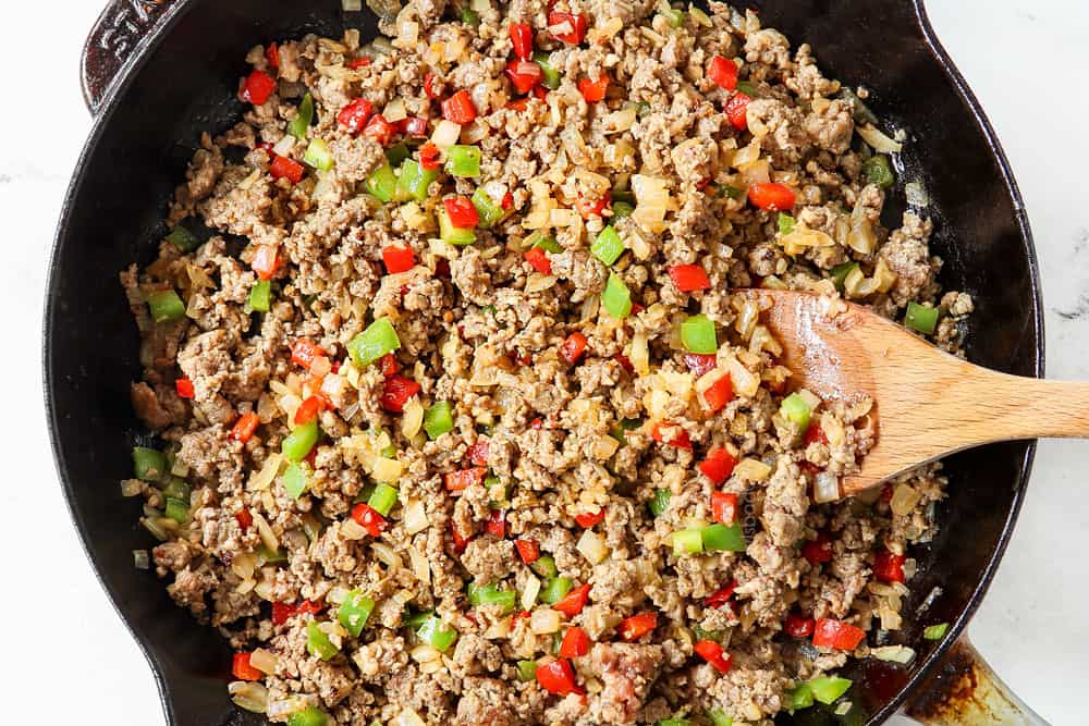 showing how to make breakfast casserole by cooking sausage, onions and bell peppers in a skillet