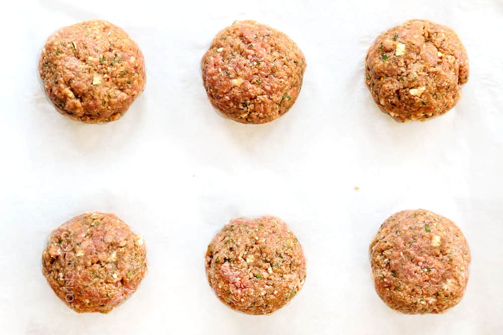 showing how to make Greek lamb burger recipe with top view of lamb burger patties and toppings: hummus, cucumbers, red onions, tomatoes, sun-dried tomatoes, tzatziki