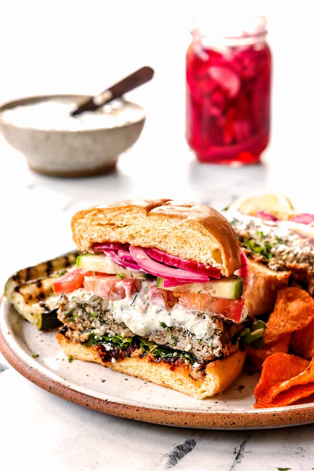 showing the inside of Greek burgers by cutting half to show lamb burger patty layered with tzatziki, cucumbers, tomatoes and red onions