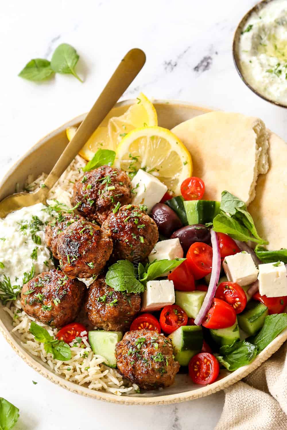 showing how to serve Greek Lamb (Keftedes) by adding to a plate with Greek salad and pitas