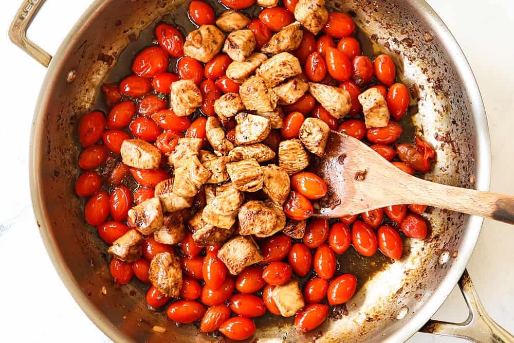 showing how to make bruschetta chicken pasta by adding the chicken and sauce to the skillet with the tomatoes