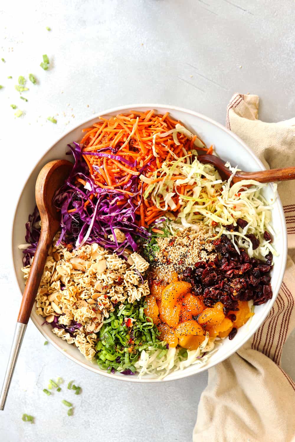 showing how to make Ramen Noodle Salad recipe by adding toasted ramen, cabbage, carrots and sesame seeds to a large white bowl