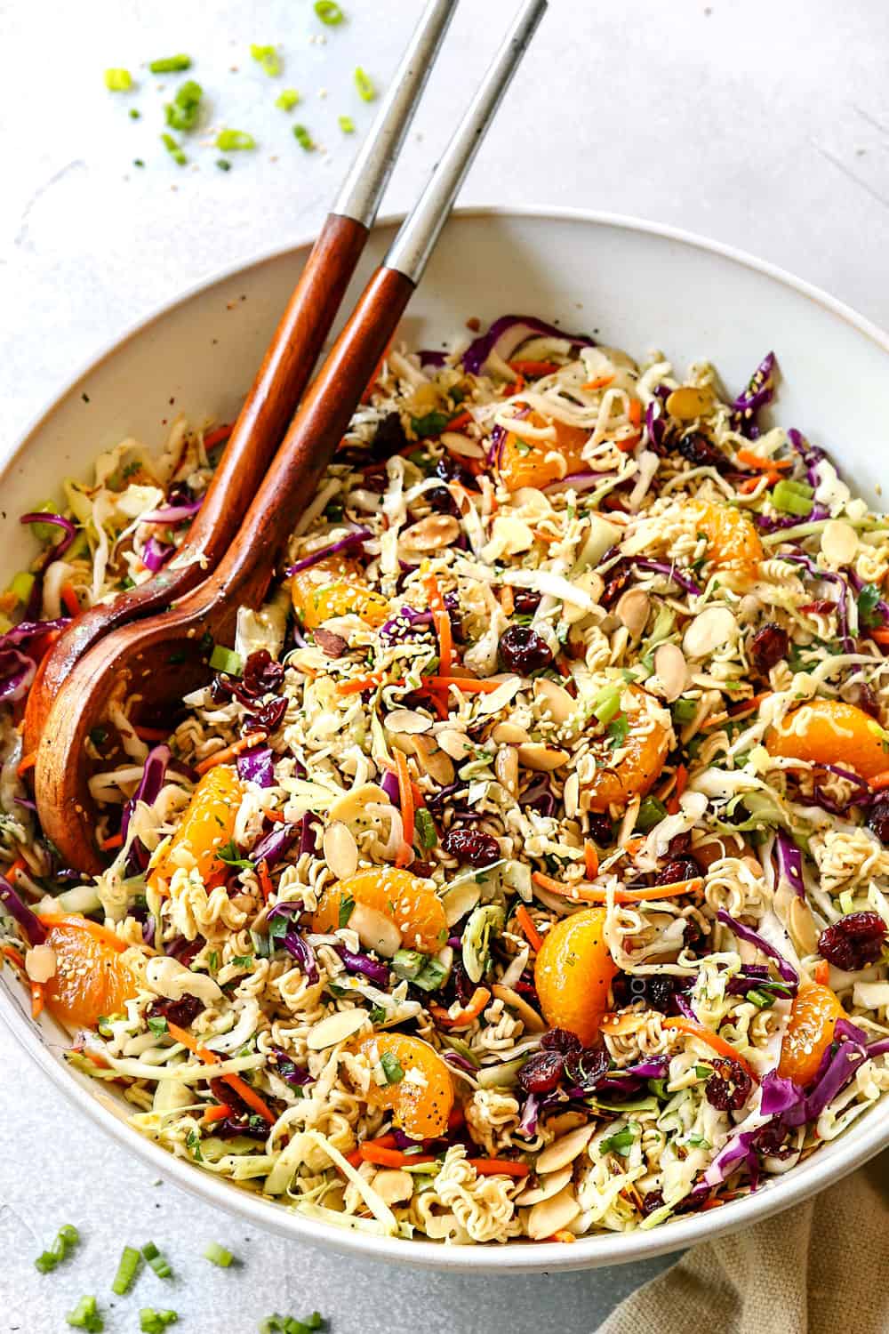 showing how to make Asian Ramen Noodle Salad by tossing the salad with the dressing in a white bowl