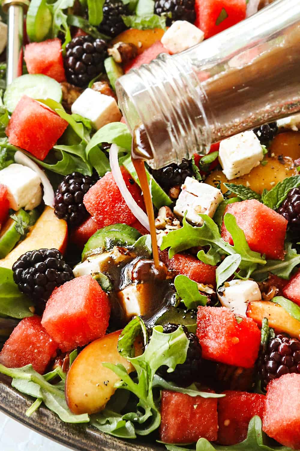 showing how to make watermelon salad recipe by drizzling with balsamic dressing