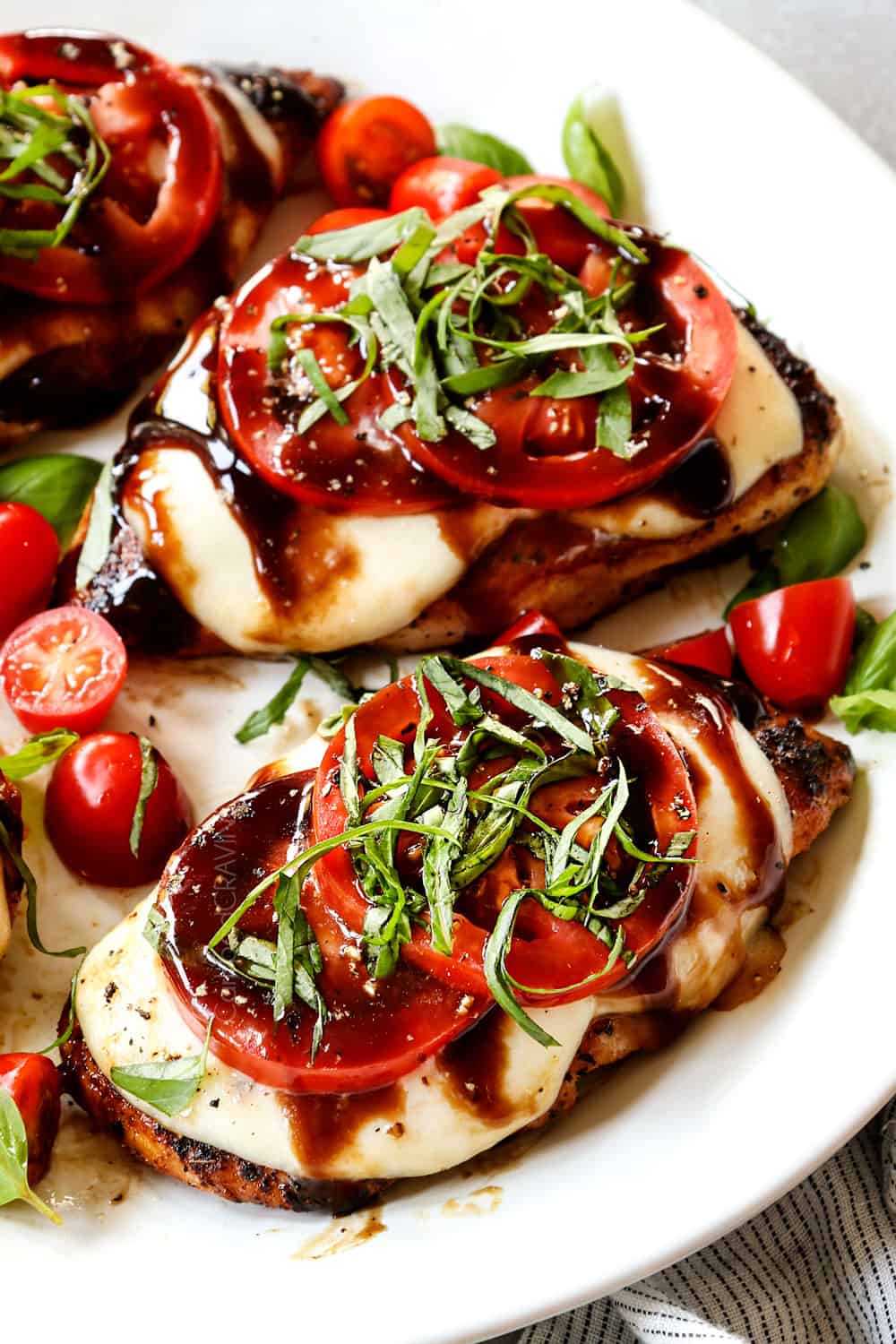 up close of chicken caprese recipe being served on a white plate with mozzarella, tomatoes, basil and balsamic reduction (balsamic glaze)