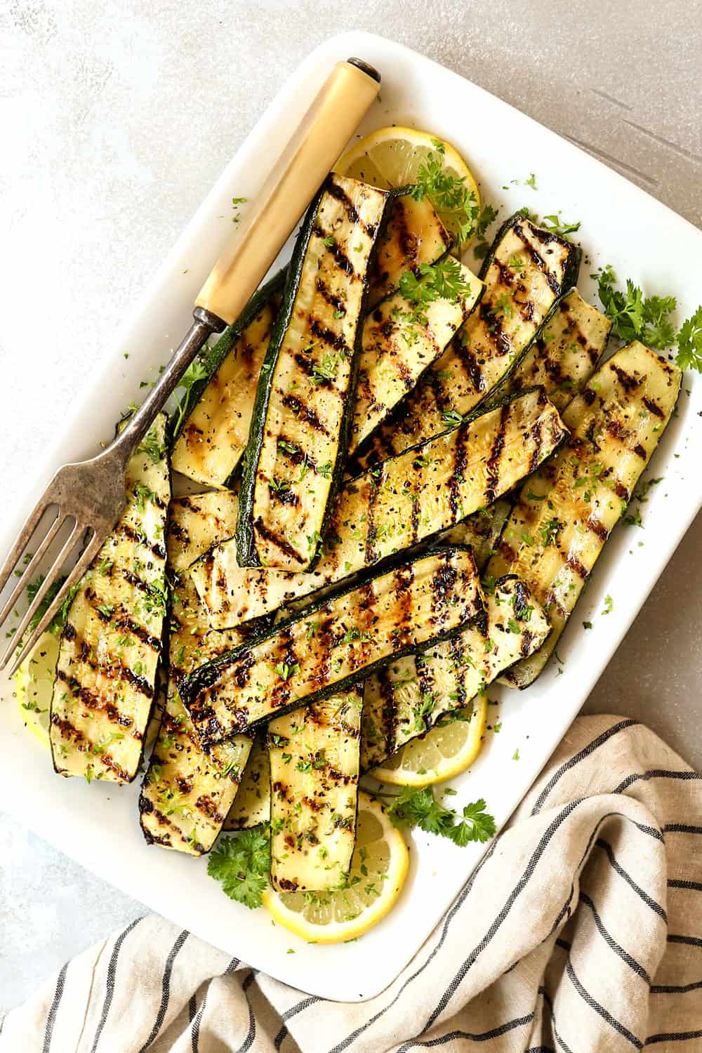 showing how to grill zucchini by adding it to a serving platter and sprinkling with fresh herbs