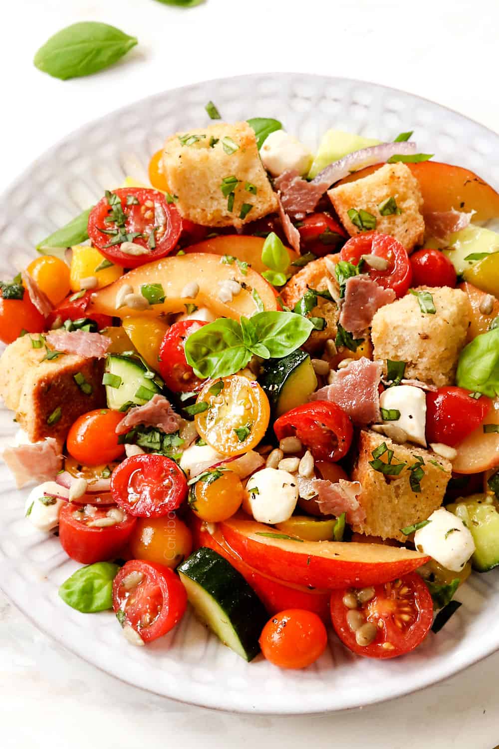 showing how how to serve panzanella salad recipe by adding to a plate and garnishing with fresh basil