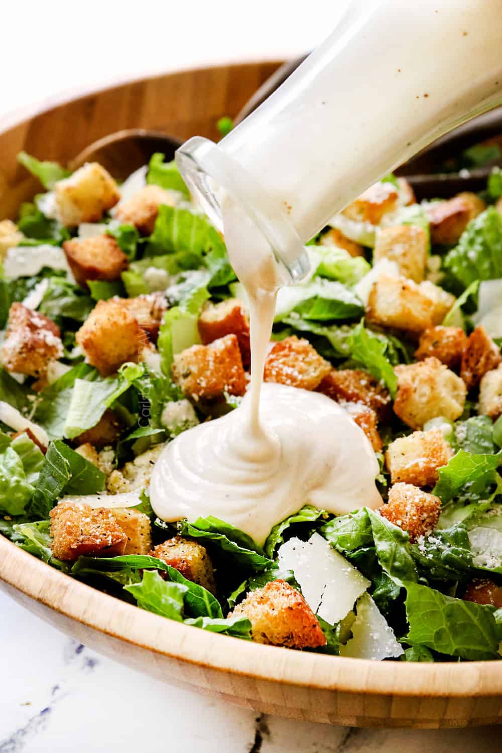 showing how to make Caesar Salad recipe by drizzling salad with Caesar Dressing