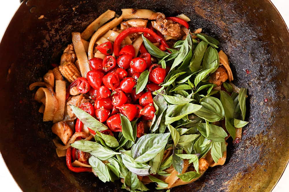 showing how to make Drunken Noodles (Pad Kee Mao) recipe by adding tomatoes, Thai basil to stir fried wide rice noodles