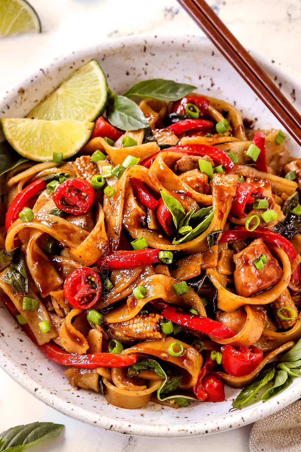 up close of Thai Drunken Noodles (Pad Kee Mao) in a white bowl with spicy and slightly sweet sauce with wide rice noodles