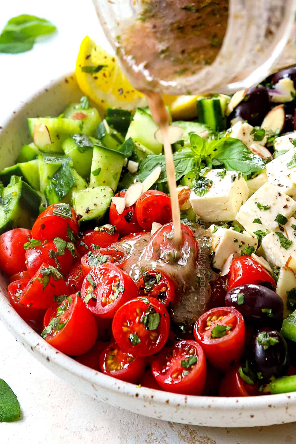 showing how to make Greek Salad by drizzling with Greek Salad Dressing