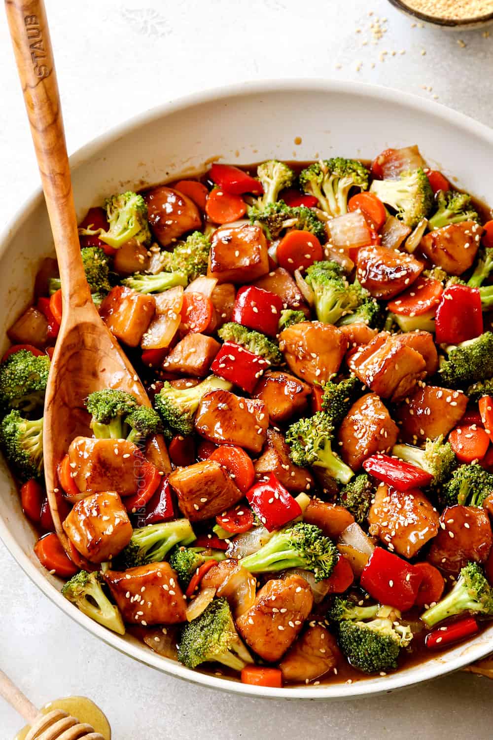 showing how to serve honey garlic chicken stir fry by garnishing with green sesame seeds in a skillet