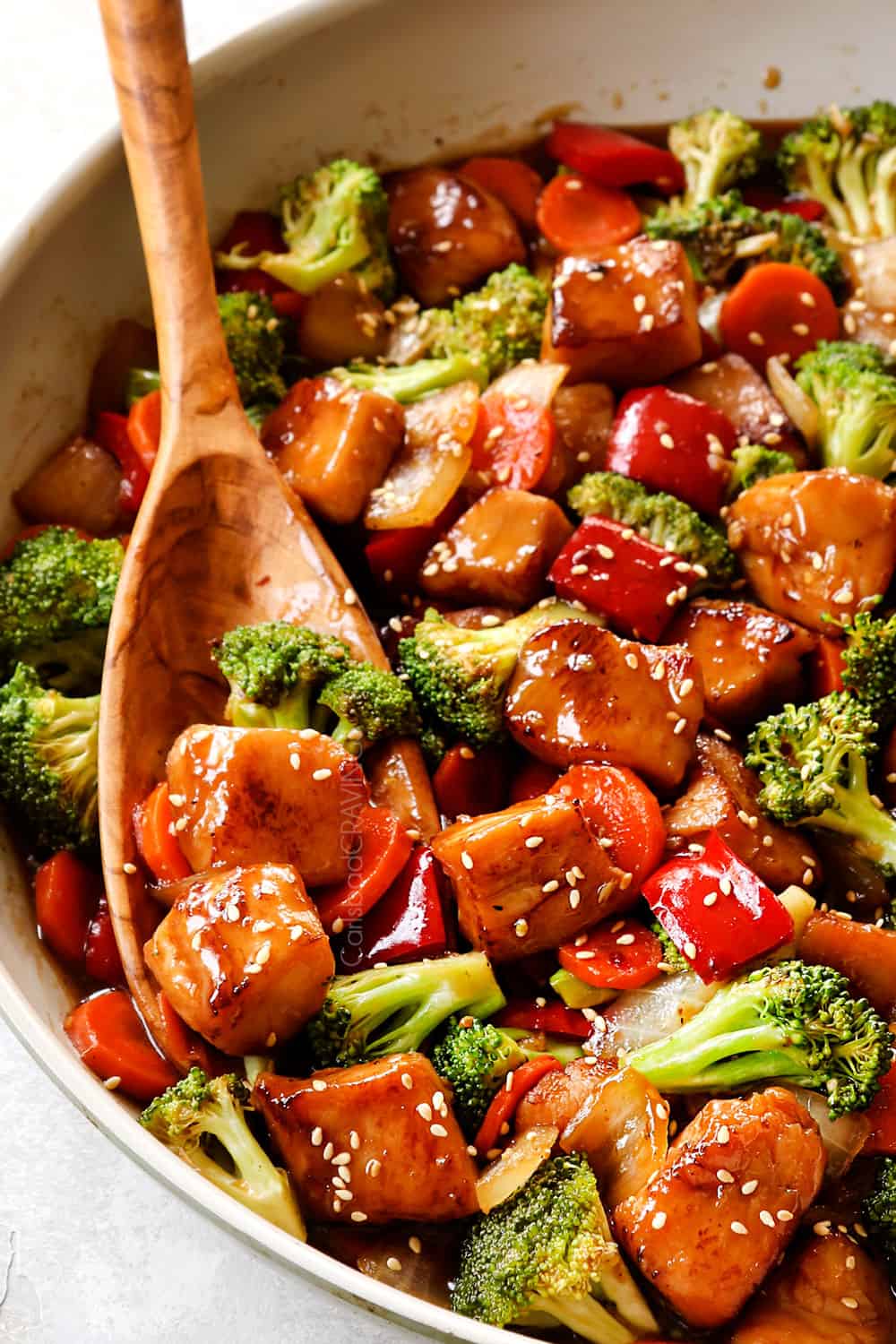 up close of Chinese honey garlic chicken in a skillet being served with a wooden spoon