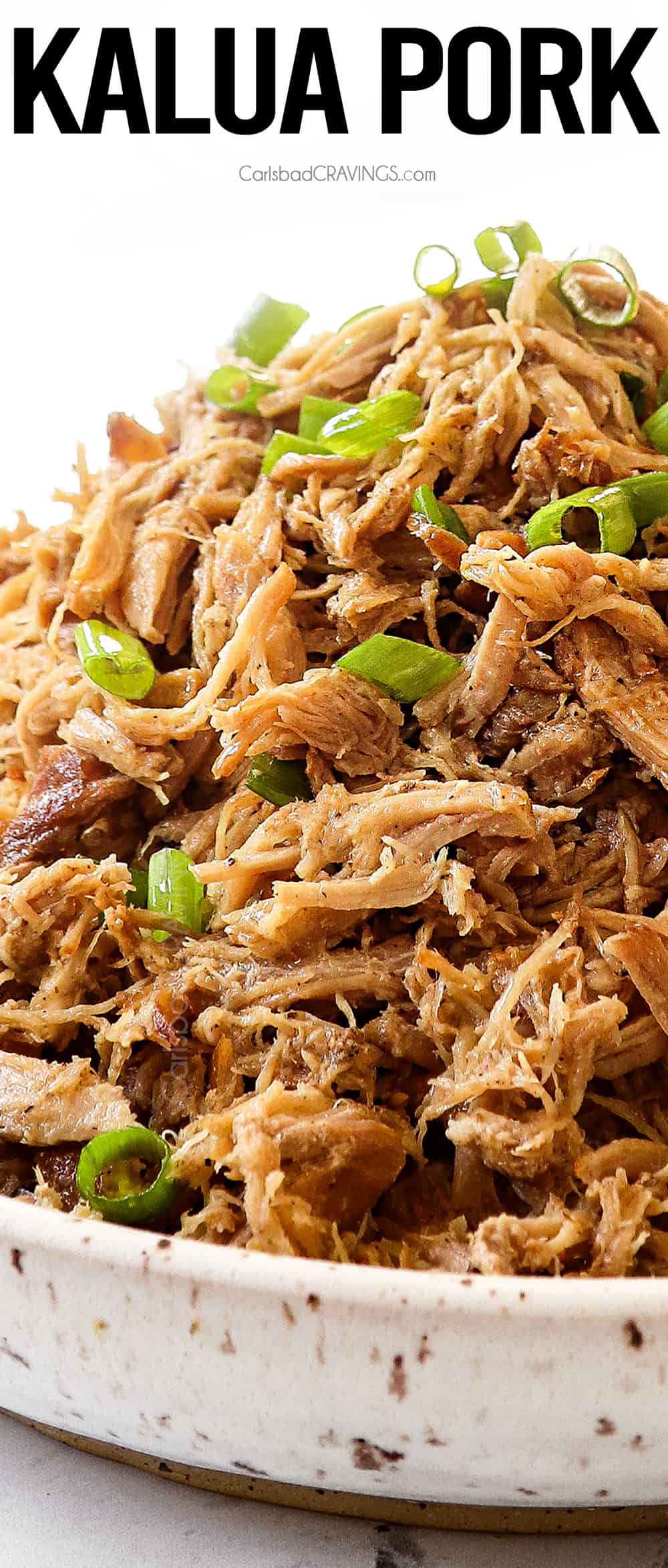 up close of a bowl of kalua pork garnished by green onions showing how tender and juicy it is