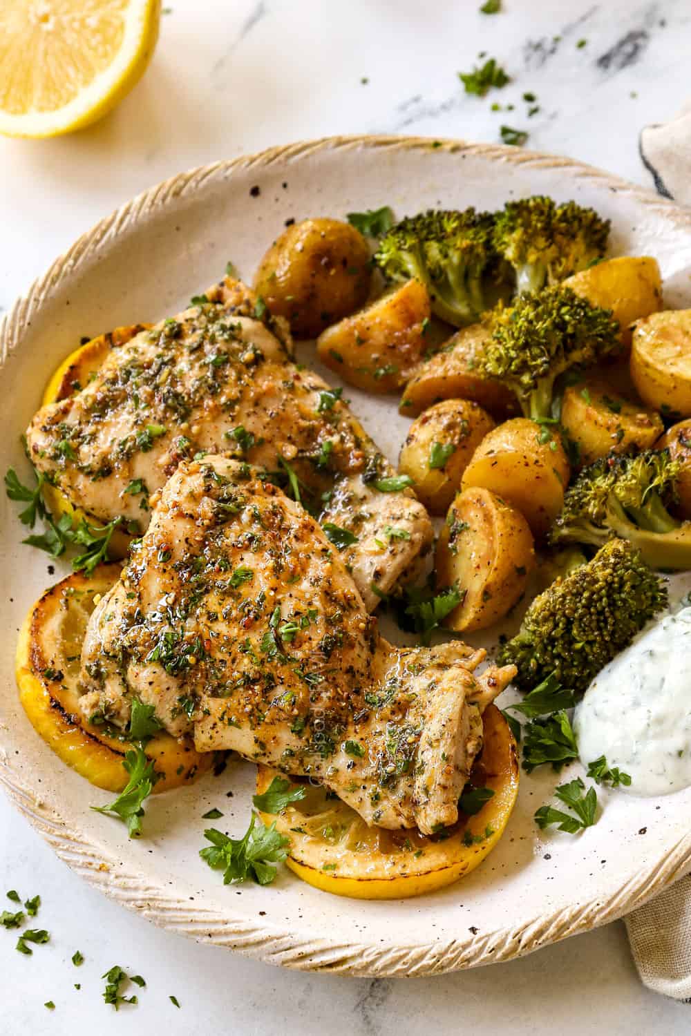 showing how to serve baked lemon garlic chicken thighs by serving on a plate with potatoes, broccoli and yogurt sauce