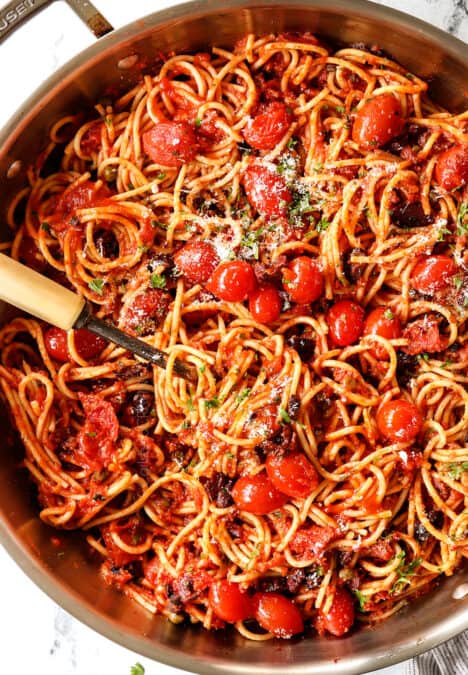top view of pasta Puttanesca with capers, Kalamata olives and anchovies in a stainless steel skillet