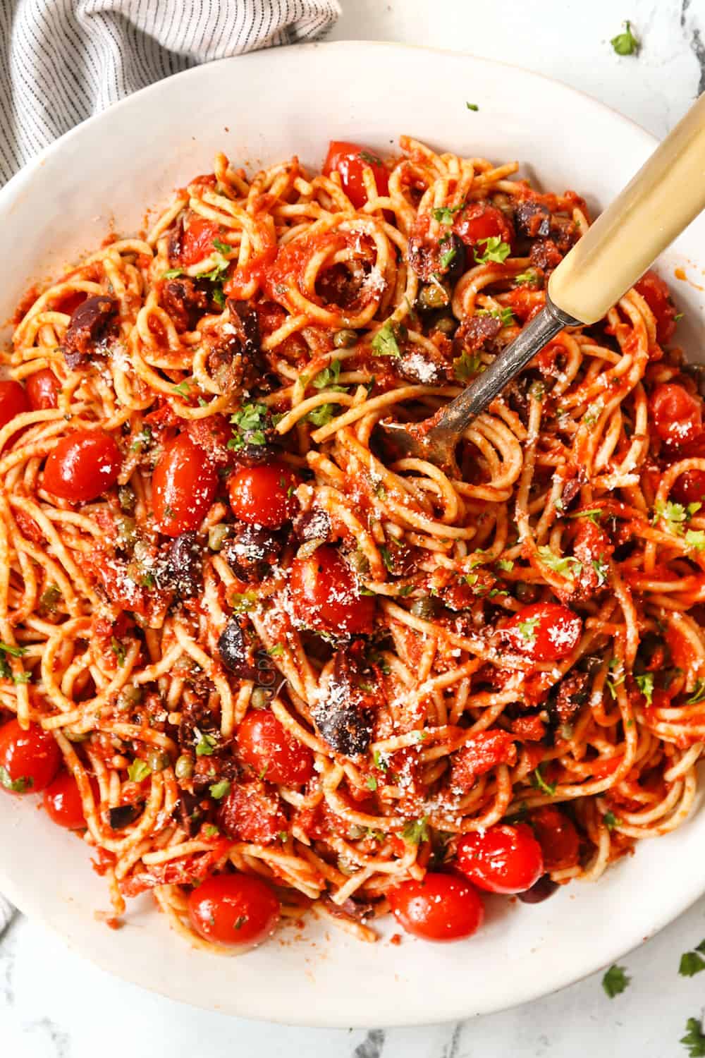 top view of pasta Puttanesca recipe on a white serving platter being served with a fork