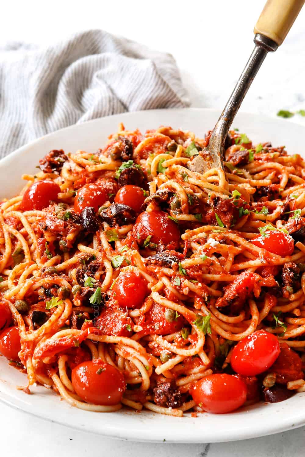 spaghetti alla Puttanesca being twirled with a fork on a serving platter