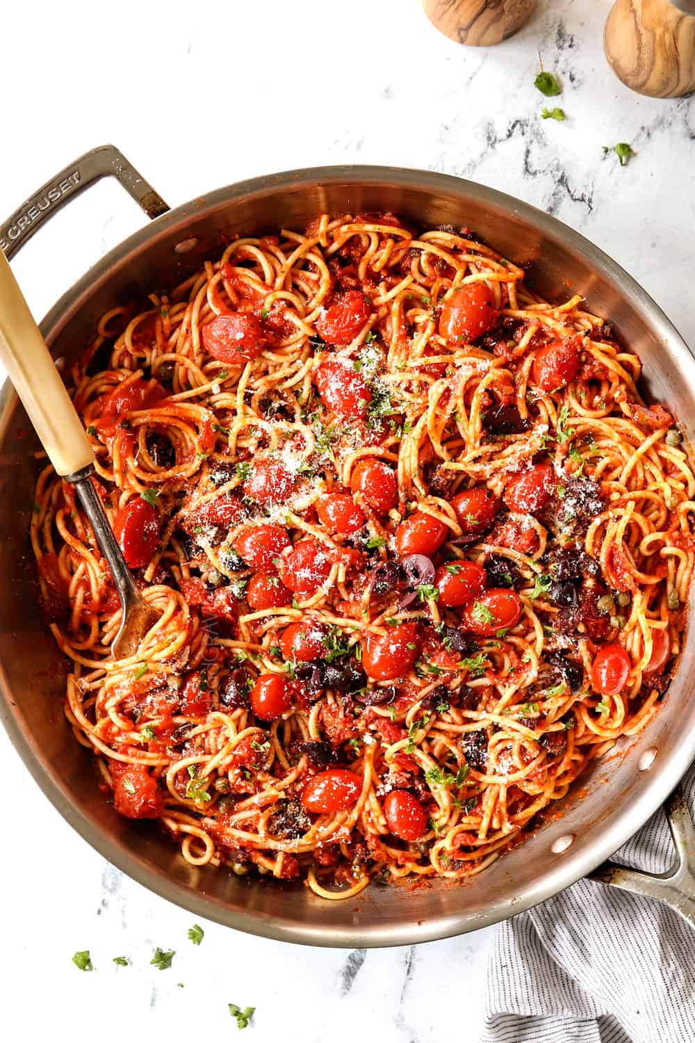 top view showing how to serve Pasta Puttanesca by garnishing with fresh parsley and Parmesan