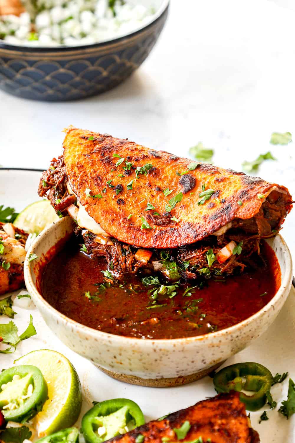 showing how to serve birria tacos with a bowl of birria consome